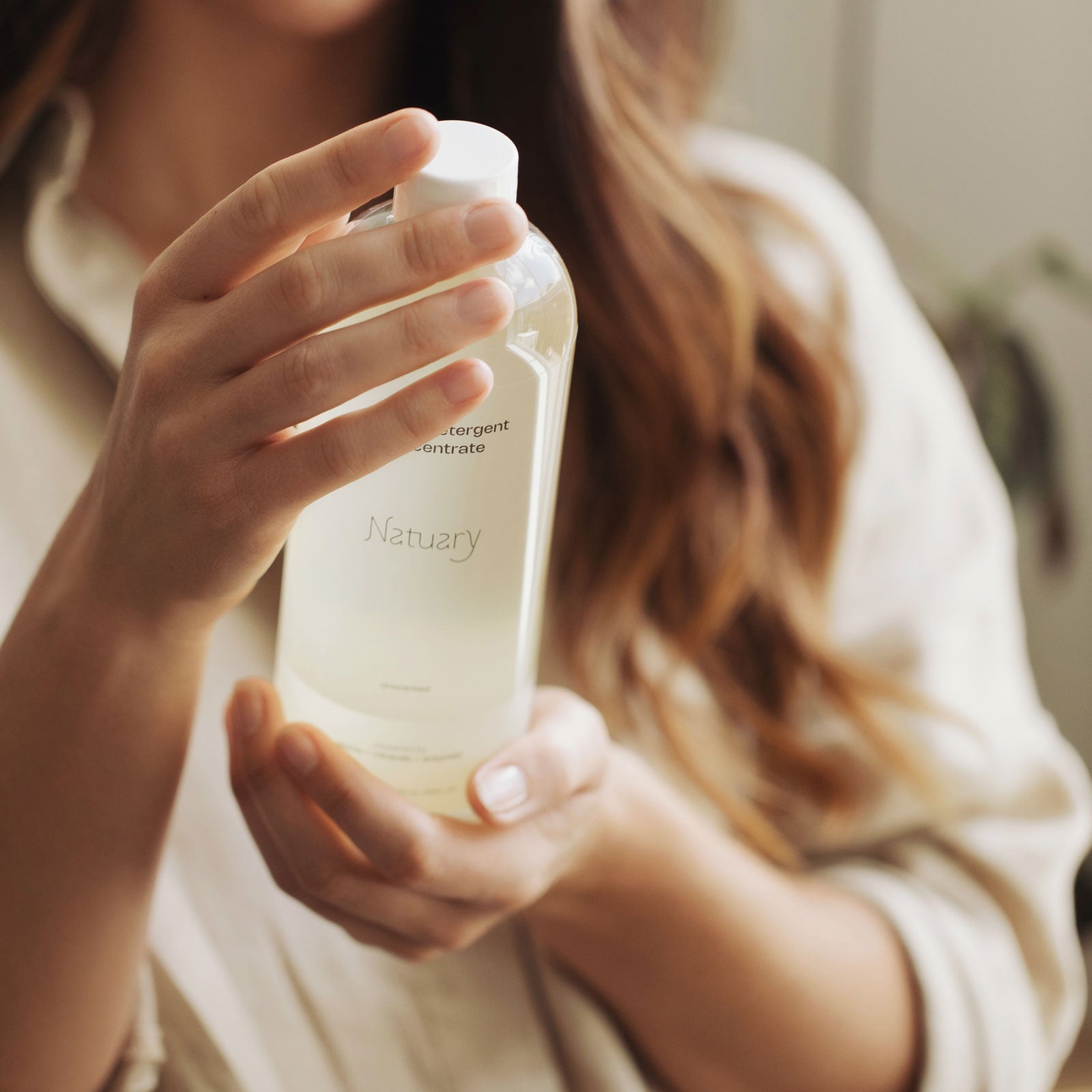 Person holding a bottle of laundry detergent concentrate with a blurred background