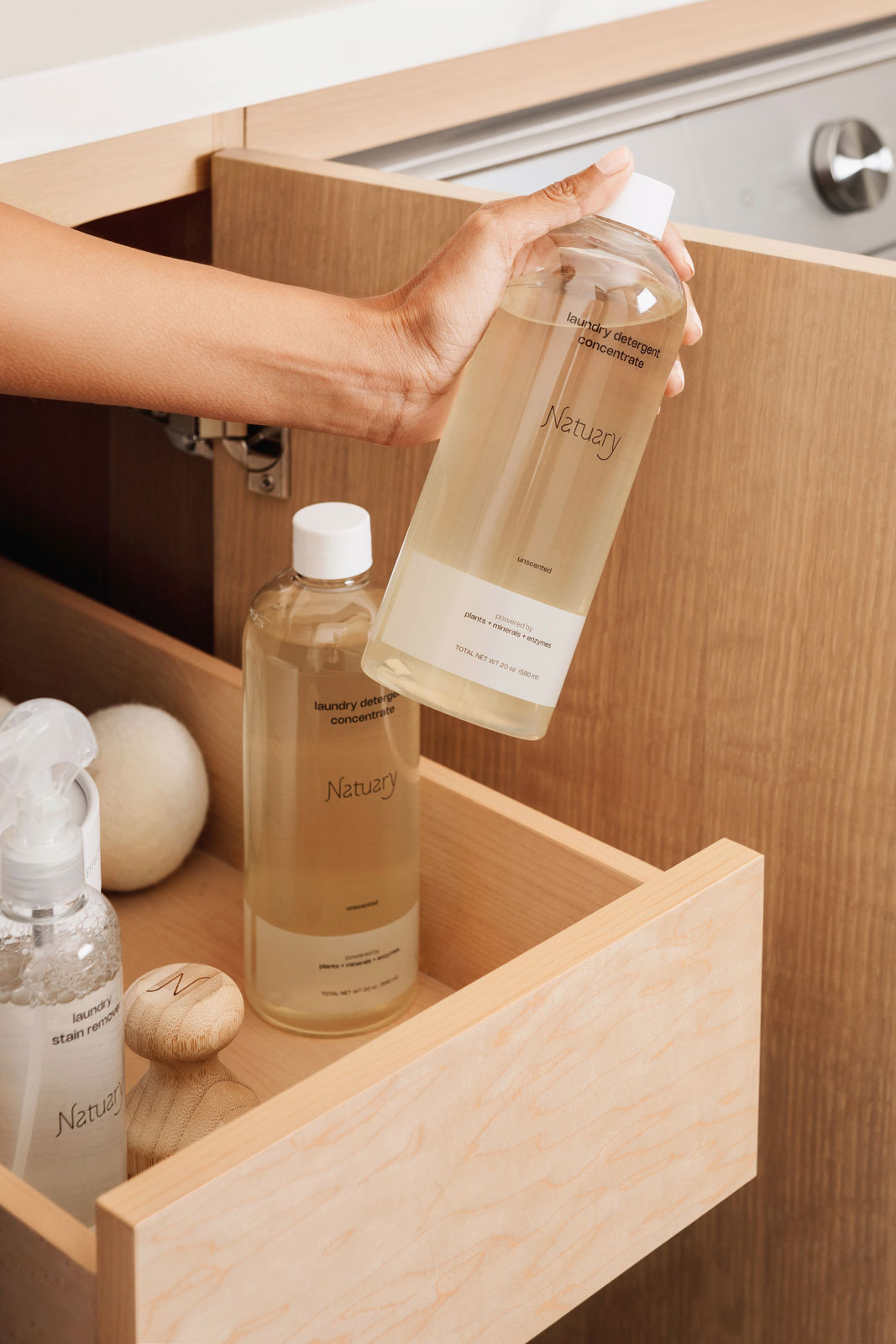Person holding a bottle labeled 'Natuary' over an open wooden cabinet with more bottles inside.
