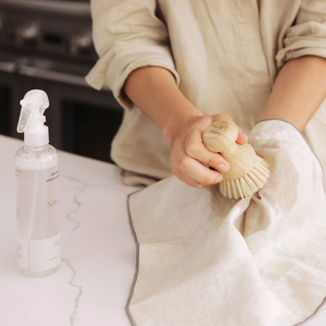 Person cleaning a pillow with a brush and spray bottle on a bed.