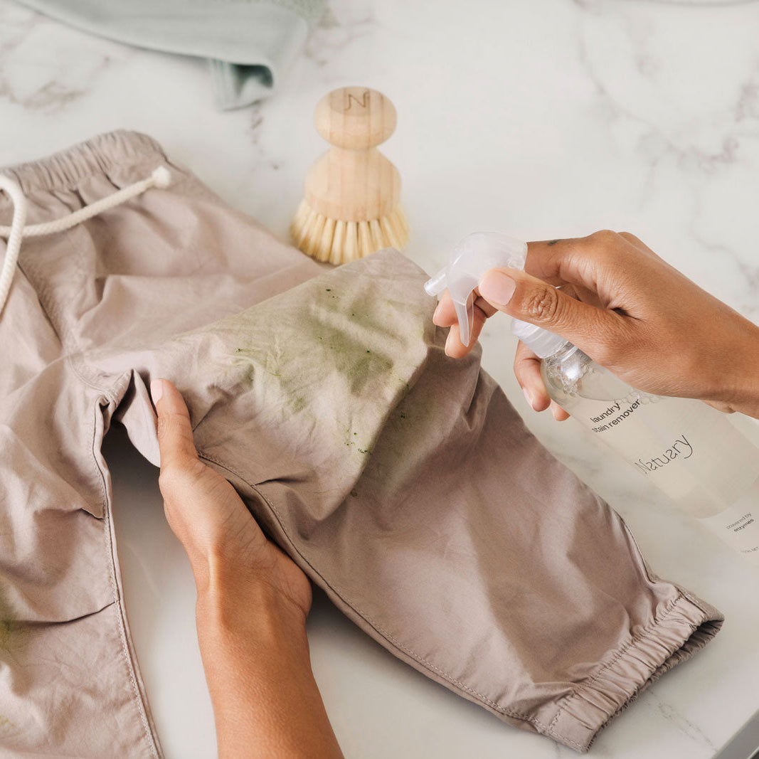 Person cleaning a pair of beige shorts with a spray bottle on a marble surface
