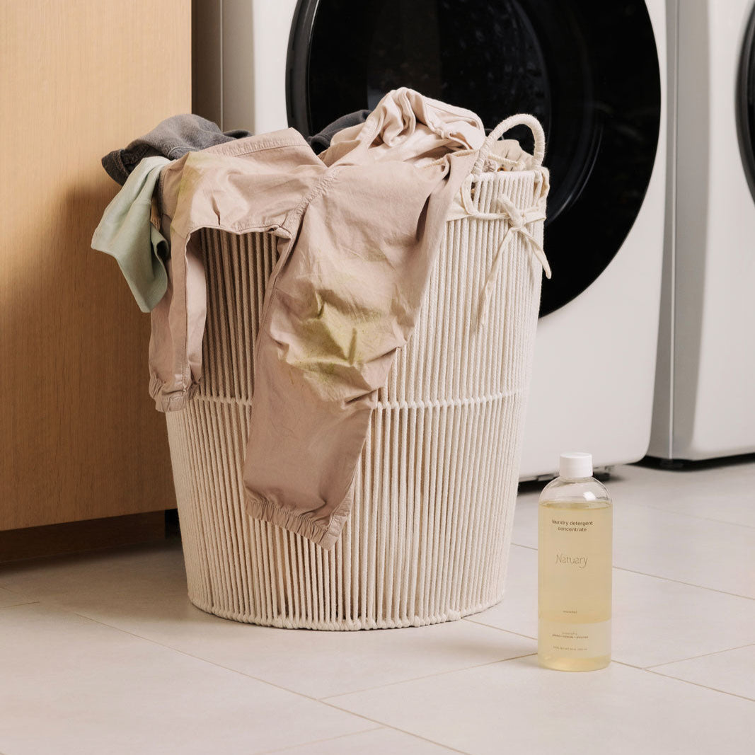 Laundry basket with clothes in front of a washing machine in a laundry room.