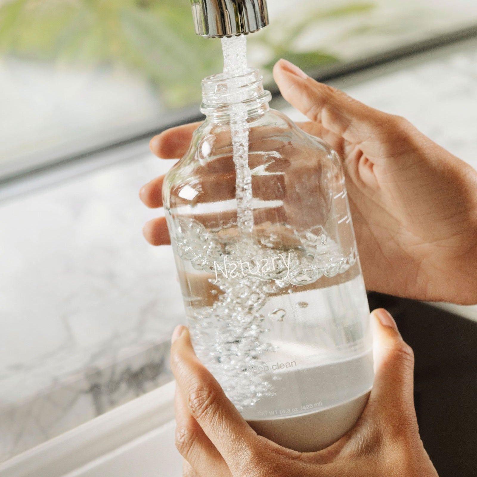 Person filling natuary bottle with water from a faucet.