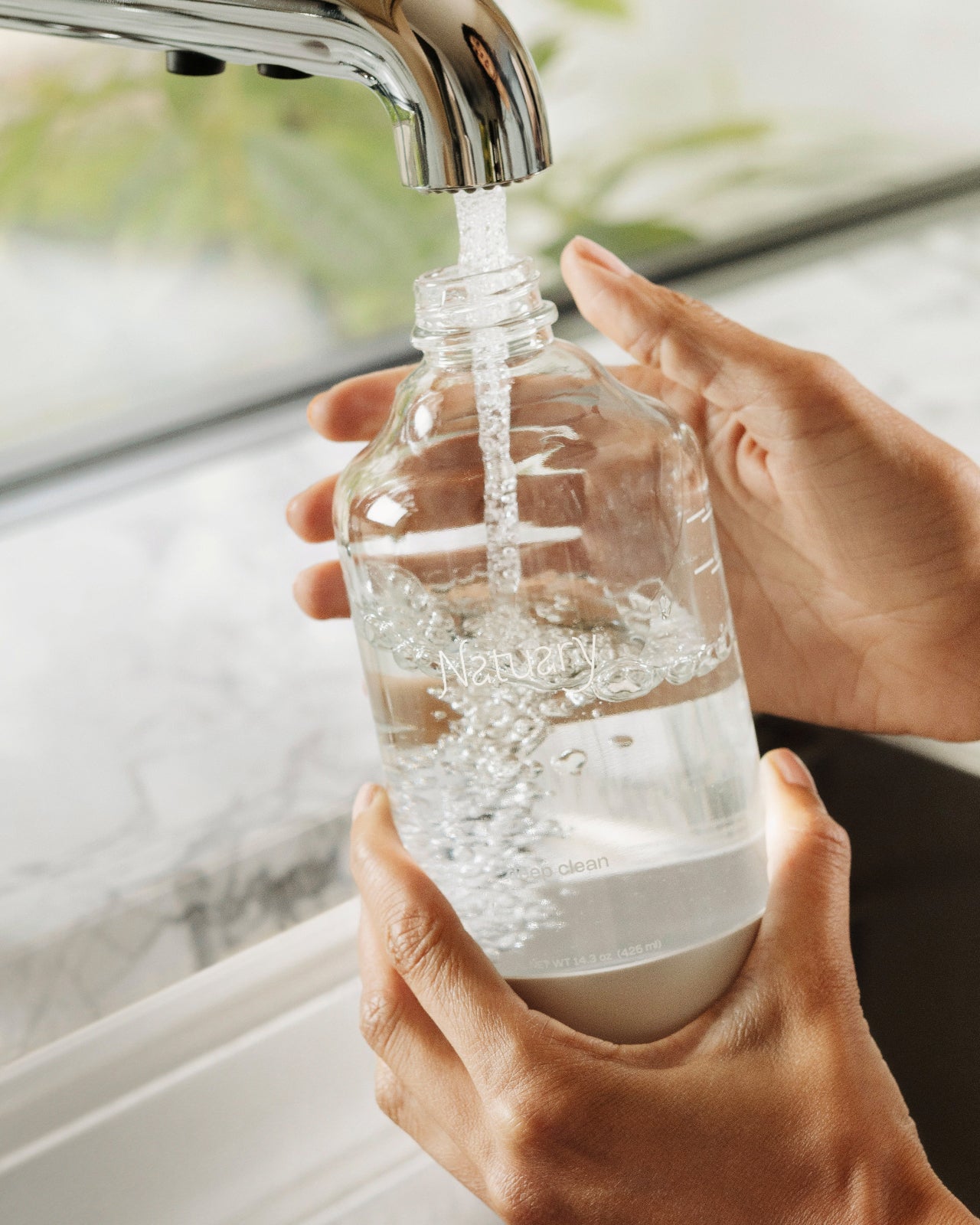 Person filling a clear bottle with water from a faucet.