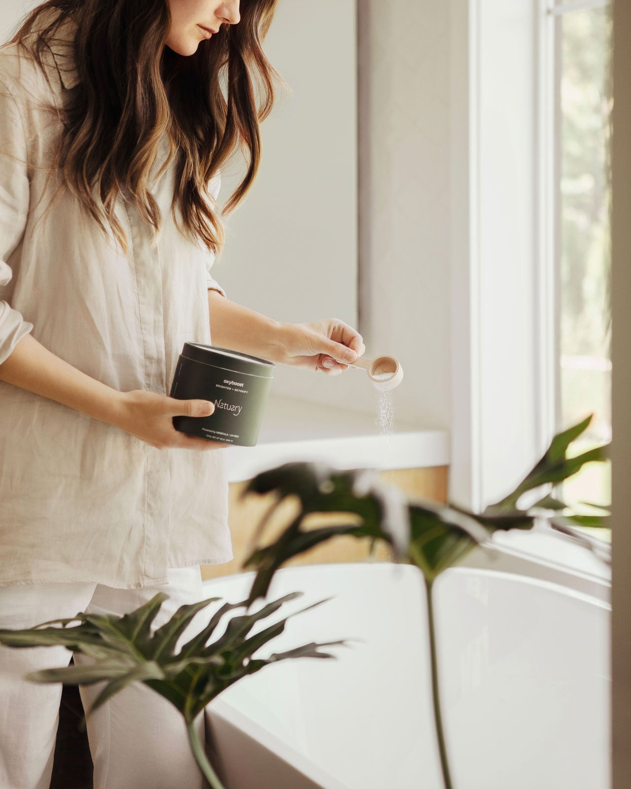 Woman pouring oxyboost into tub with plants in the foreground