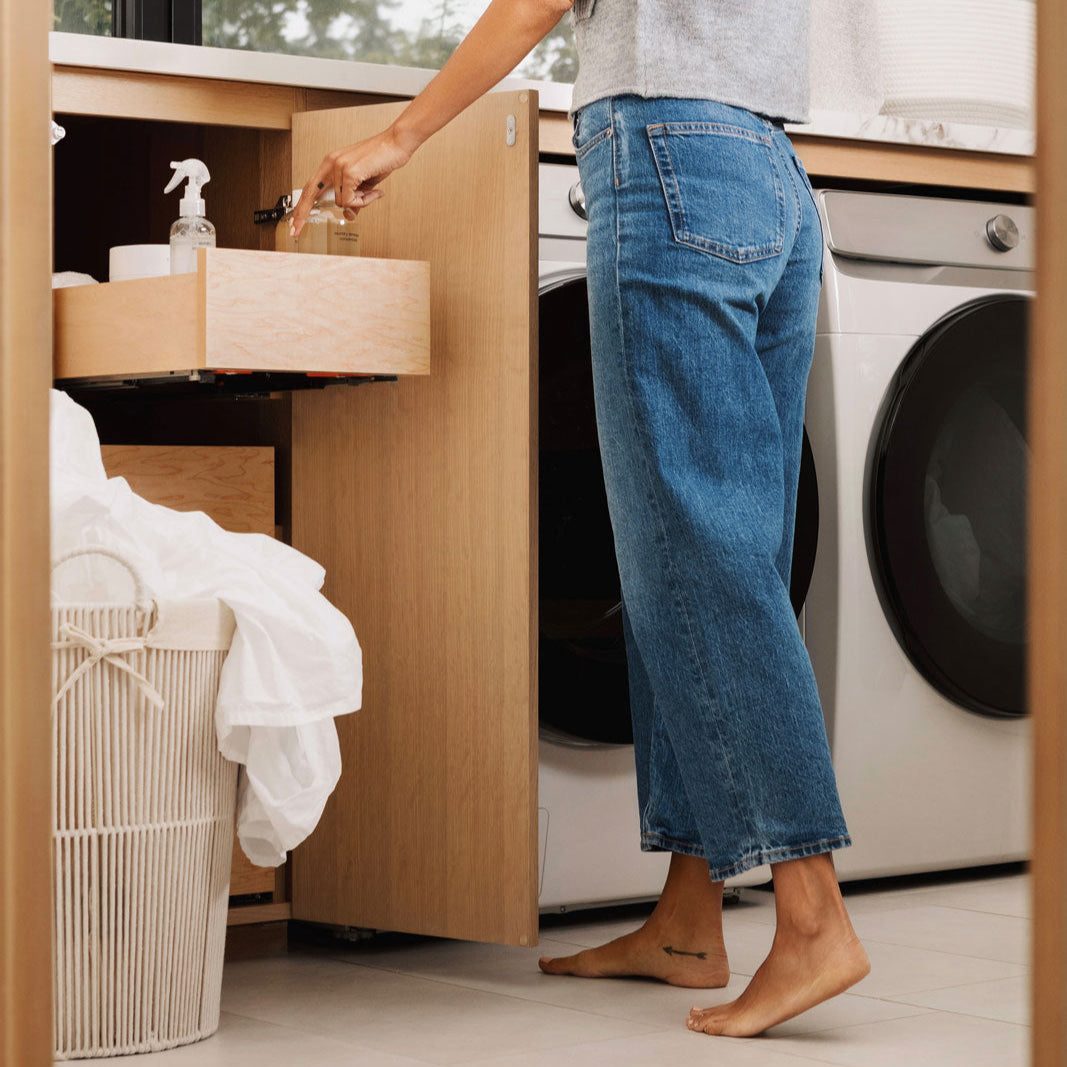 Person organizing laundry in a kitchen with washing machine and dryer.